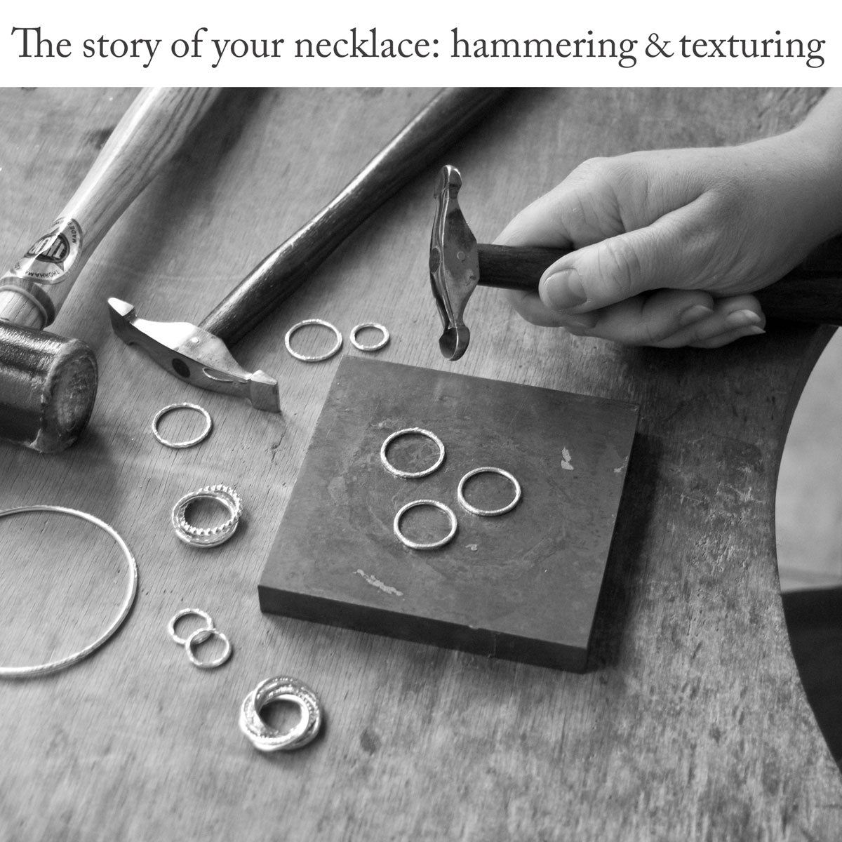 Close-up of silversmith sitting at a workbench using a metal-stamping block and several hammers with different heads to apply texture to a collection of silver rings with the headline text 'The story of your necklace: hammering and texturing'