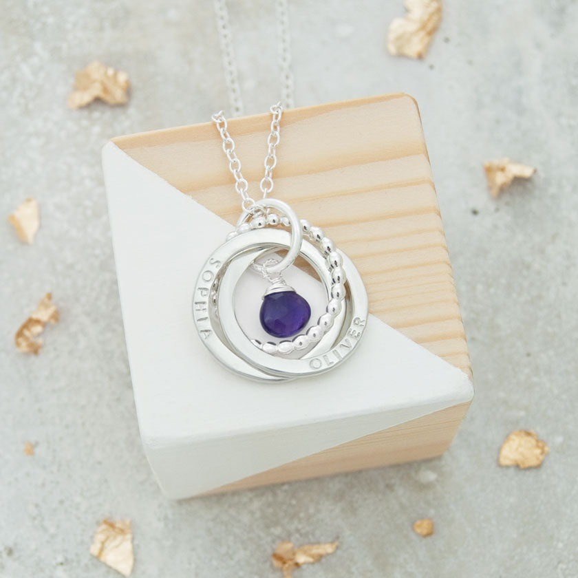 personalised russian ring necklace with purple birthstone on wooden block with gold leaf in background